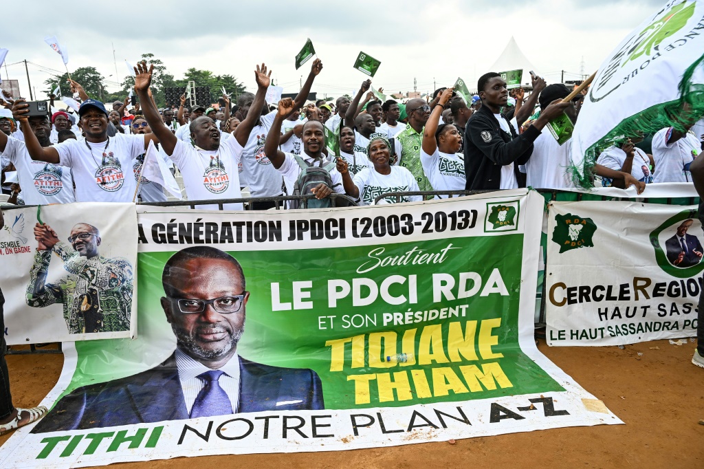 Des partisans de la Coalition pour une alternance pacifique à côté d'une banderole politique du président du Parti démocratique de Côte d'Ivoire (PDCI), Tidjane Thiam, le 31 mai 2025 à Abidjan, avant l'élection présidentielle du 25 octobre 2025.