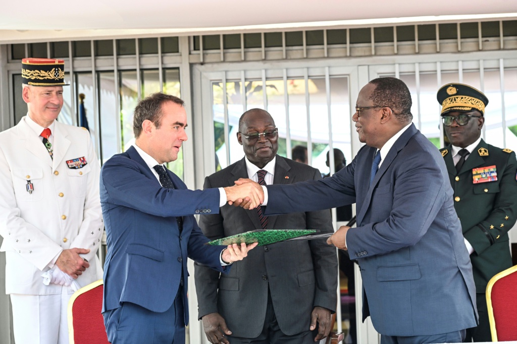 Le ministre ivoirien de la Défense, Téné Birahima Ouattara (2e d), et le ministre français des Forces armées, Sébastien Lecornu (2e g), se serrent la main après avoir signé un document au camp militaire "général Ouattara Thomas d'Aquin", ancienne base du 43e bataillon d'infanterie de marine française à Port-Bouët, le 20 février 2025 à Abidjan.