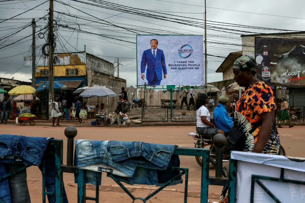 Des piétons passent devant un panneau publicitaire représentant le Président camerounais Paul Biya, dans une rue de Yaoundé, le 28 octobre 2025, au lendemain de l'annonce des résultats de l'élection présidentielle au Cameroun.
