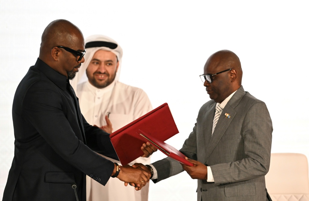 Le représentant de la RDC, Sumbu Sita Mambu (g), et le représentant du Groupe armé M23, Benjamin Mbonimpa (d), se serrent la main après la signature d'un accord de paix global, en présence du négociateur en chef du Qatar Mohammed al-Khulaifi (c), le 15 novembre 2025 à Doha.