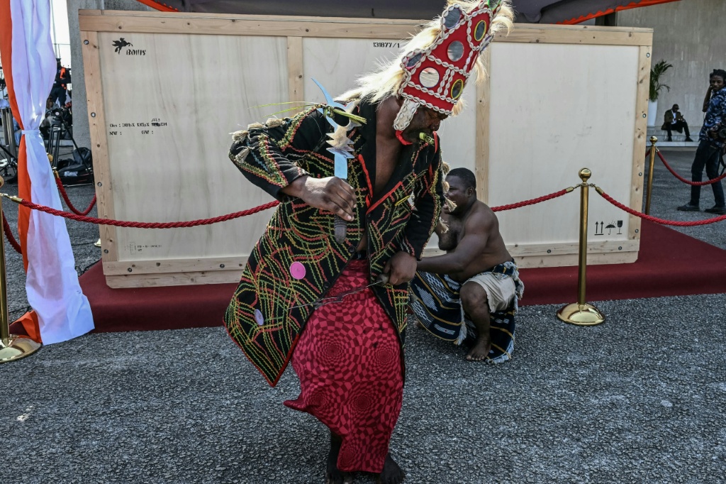 Un danseur traditionnel devant la caisse de transport du tambour parleur Djidji Ayokwe, restitué par la France, à son arrivée à l'aéroport international d'Abidjan, le 13 mars 2026 en Côte d'Ivoire.
