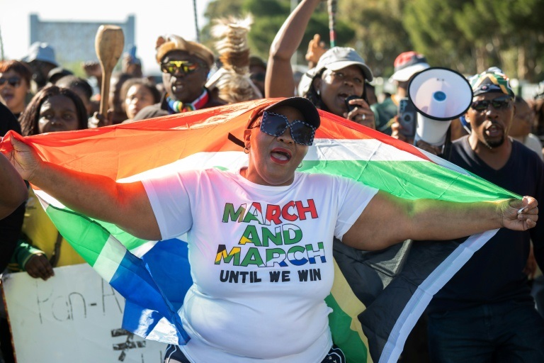 Une femme, portant un t-shirt orné du logo de 'March and March', tient un drapeau sud-africain lors d'une manifestation contre les immigrants illégaux à Goodwood, en banlieue du Cap, le 30 mai 2026 en Afrique du Sud.