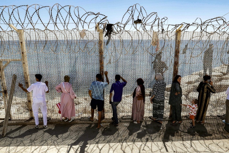 Des personnes attendent derrière une clôture surmontée de barbelés le retour de proches ayant tenté de franchir la frontière pour entrer dans l’enclave espagnole de Ceuta, le 2 août 2026 à Fnideq.